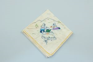 Image of Okiaksak: two figures heating kettle over fire, one of a set of 2 embroidered napkins with seasons Operngak and Okiaksak